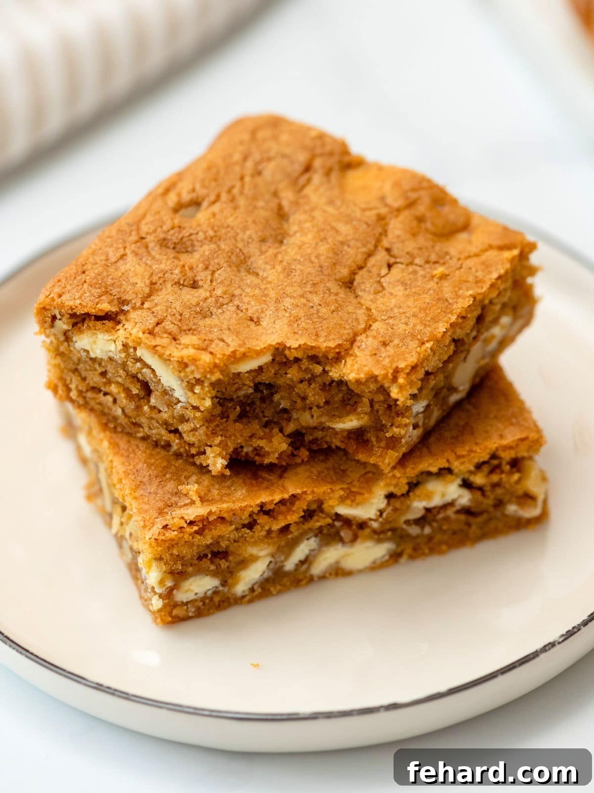 Two soft, chewy Brown Butter Blondies, enriched with white chocolate chips and walnuts, perfectly cut into squares and arranged invitingly on a white plate. Each blondie showcases its signature crinkly top and golden-brown edges.