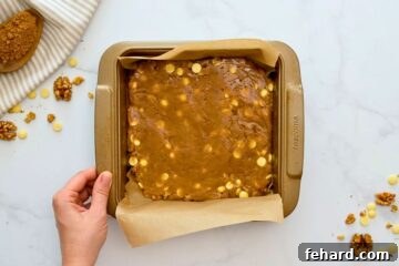 Blondie batter with white chocolate chips spread out evenly in a baking dish lined with parchment paper, prepared for baking.