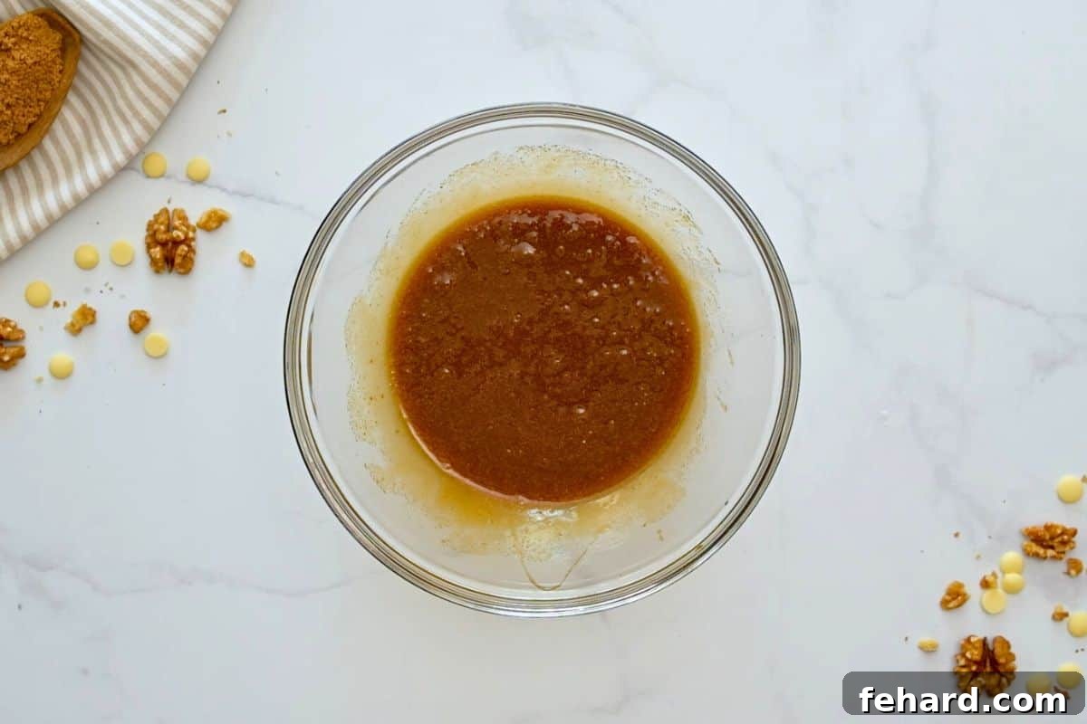 A large mixing bowl containing the perfectly combined browned butter, brown sugar, vanilla, and egg, whisked to a smooth, inviting consistency before flour is added.