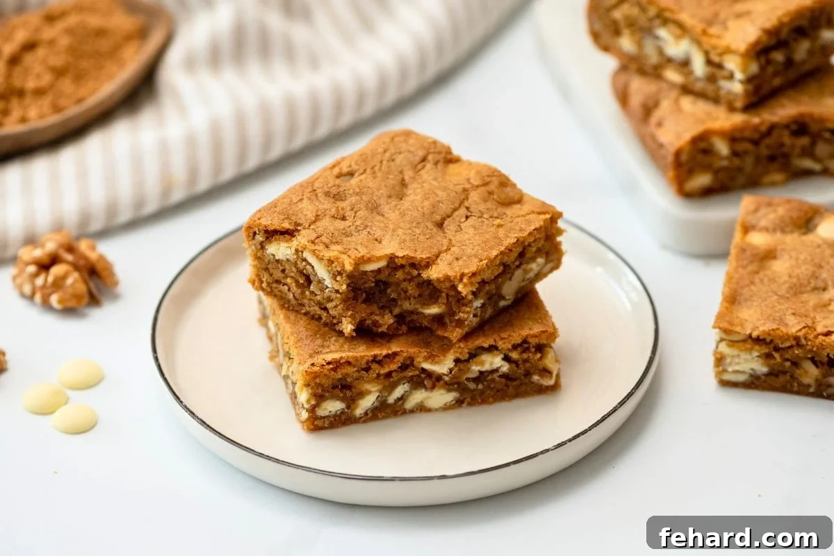Two perfectly cut squares of Browned Butter Blondies, featuring delightful white chocolate chips and walnuts, elegantly presented on a plate, ready to be enjoyed as a decadent dessert.