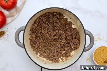 Beef browned with onion, garlic, and dried seasonings in large stock pan next to brown rice for stuffed pepper casserole.