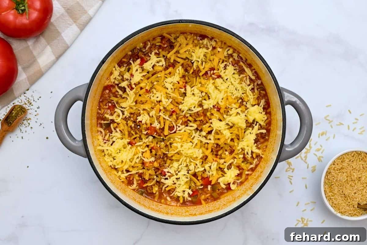 One Pot Stuffed Bell Pepper Casserole with Cheese Stuffed Pepper Casserole with rice in a large stock pan, topped generously with a mix of shredded cheddar and mozzarella cheese before melting.