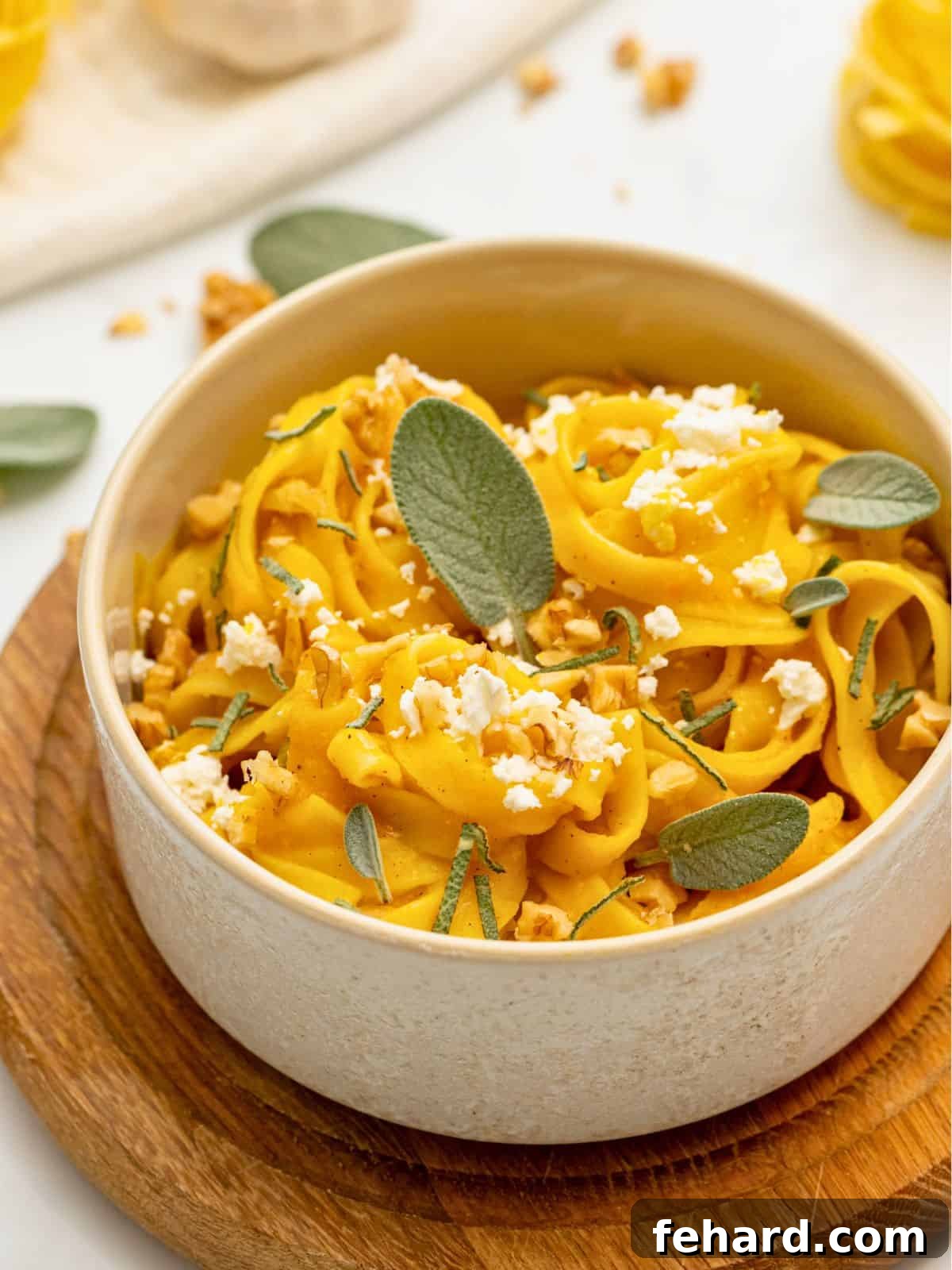 Fettuccine tossed with rich brown butter pumpkin pasta sauce served in a rustic dish, garnished with crumbled goat cheese, fresh sage leaves, and chopped walnuts, highlighting its autumn appeal.