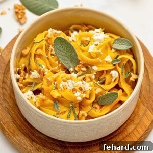 Fettuccine tossed with pumpkin pasta sauce served in white dish topped with crumbled goat cheese, sage, and chopped walnuts.