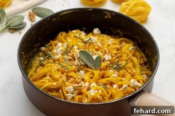 Fettuccine tossed with pumpkin pasta sauce in skillet topped with crumbled goat cheese, sage, and chopped walnuts.
