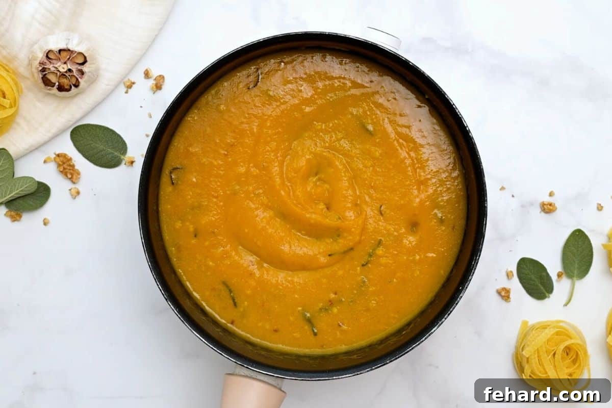 A saucepan filled with a rich, vibrant pumpkin pasta sauce, featuring the warm hues of pumpkin puree, nutty brown butter, and fresh sage leaves.