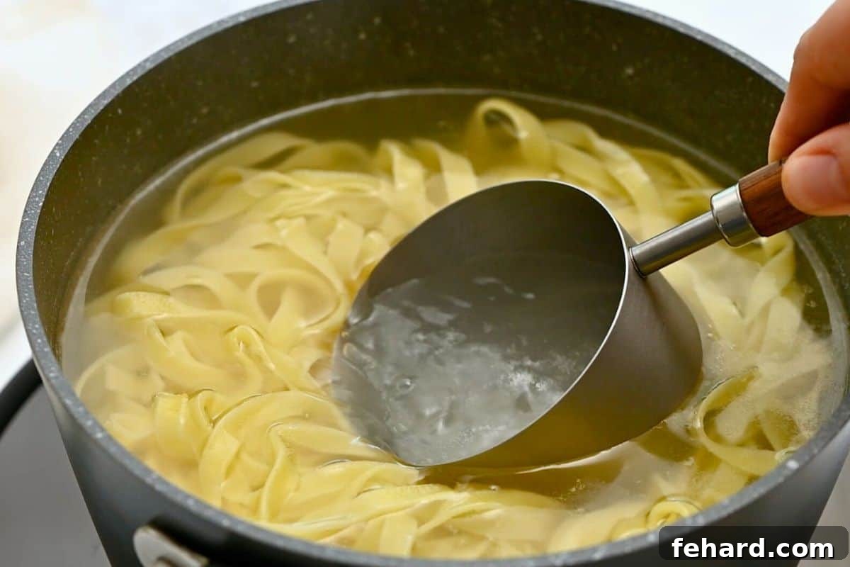 A clear measuring cup carefully scooping up starchy pasta water from a pot of boiling fettuccine noodles, an essential step for a perfect sauce.