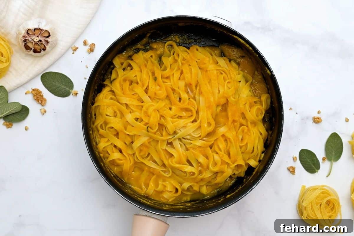 Fettuccine noodles, perfectly cooked, being generously tossed with the rich brown butter pumpkin sauce in a skillet, ensuring every strand is coated.
