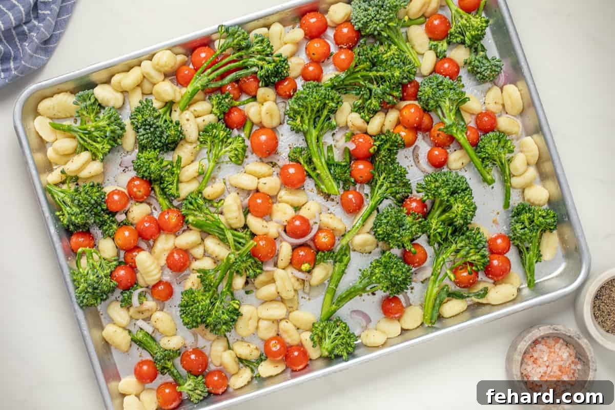 Potato gnocchi, broccolini, and grape tomatoes tossed with olive oil garlic powder, red pepper flakes, and oregano, ready for roasting on a sheet pan.