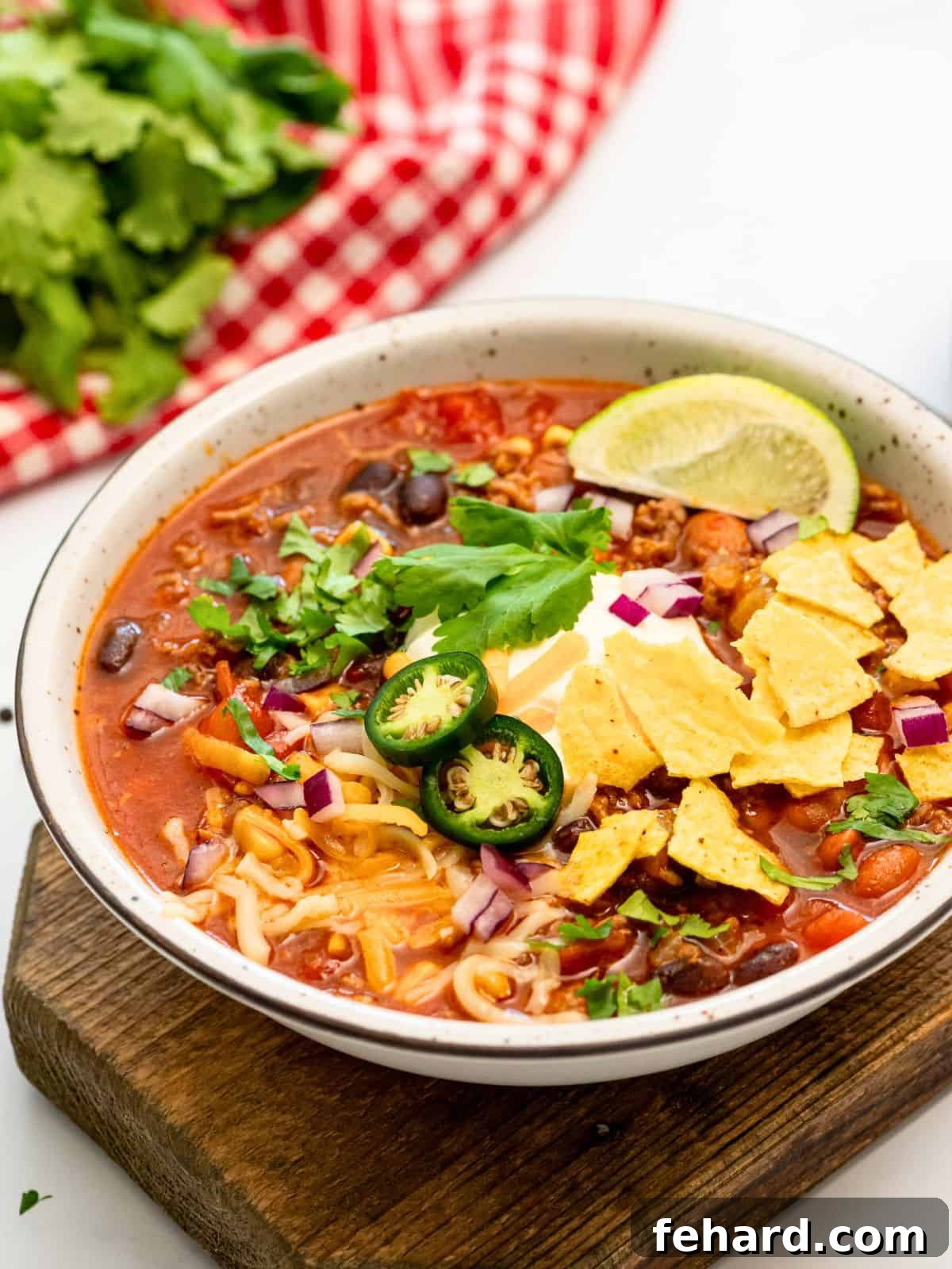 A vibrant bowl of stovetop taco soup featuring ground beef, corn, and beans, elegantly garnished with a dollop of sour cream, a fresh lime wedge, chopped cilantro, and crispy tortilla chips.