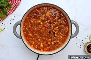 Large soup pan filled with pinto beans, black beans, corn, tomatoes, and ground beef for taco soup.