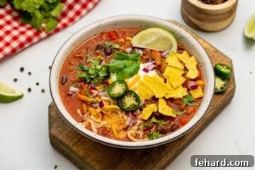 Bowl of homemade taco soup made with ground beef, corn, and beans topped with sour cream, lime, cilantro, jalapeno, onions, and tortilla chips.