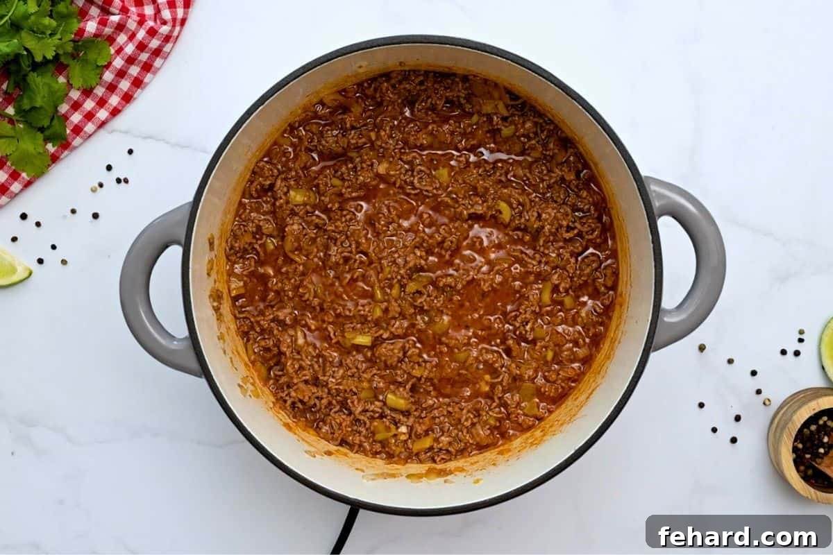 Taco meat simmering with tomato sauce in a large soup pan, creating a rich and flavorful foundation for the soup.