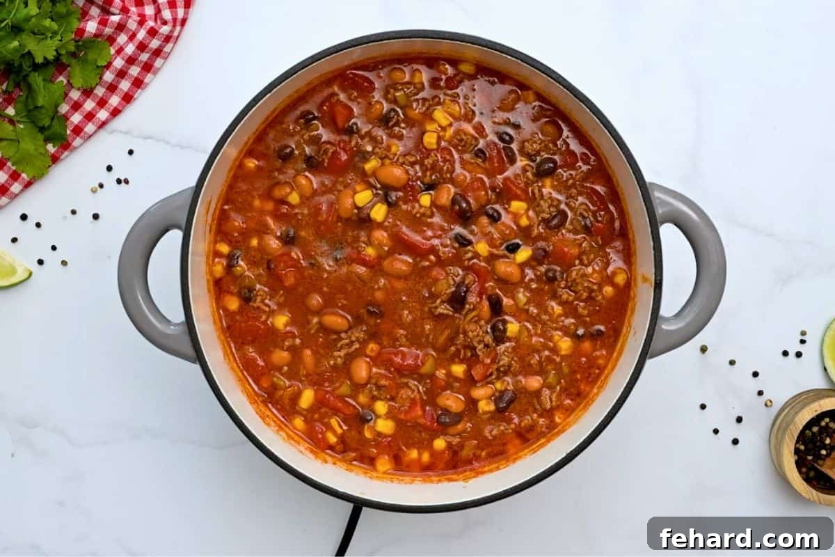 A large soup pan filled with pinto beans, black beans, corn, diced tomatoes, and ground beef, ready to simmer into a delicious taco soup.