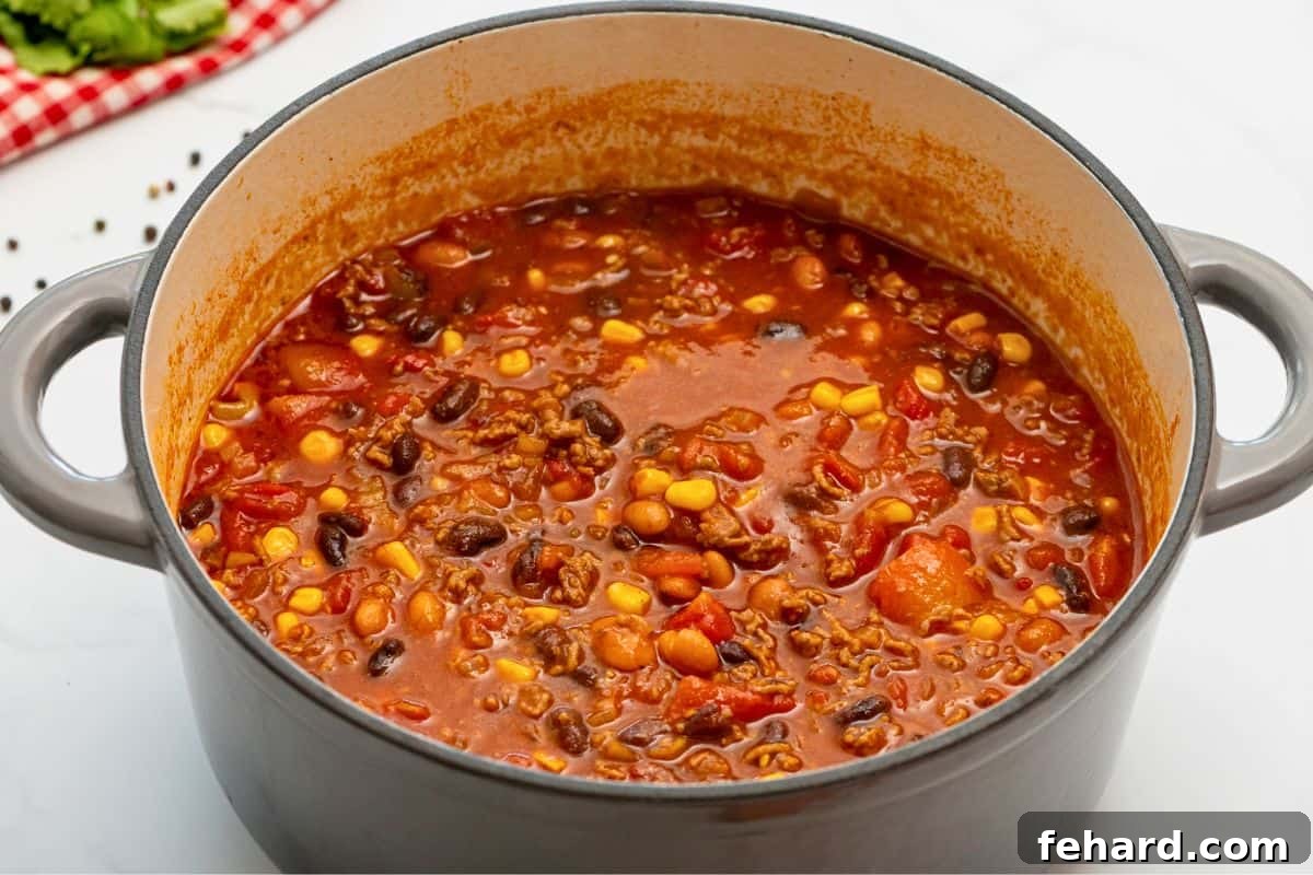 A large soup pan filled with homemade taco soup, featuring ground beef, beans, corn, and tomatoes, simmering gently on the stovetop.