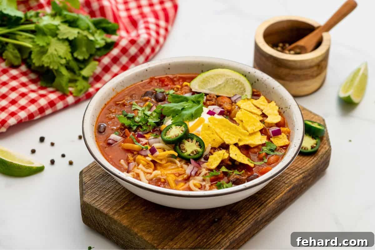 A beautifully presented bowl of easy taco soup, generously topped with a lime wedge, sour cream, fresh cilantro, sliced jalapeños, red onions, and crispy tortilla chips.