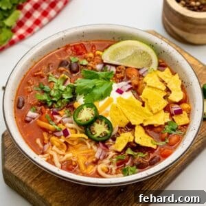 Bowl of easy taco soup made with ground beef, corn, and beans topped with sour cream, lime, cilantro, jalapeno, onions, and tortilla chips.