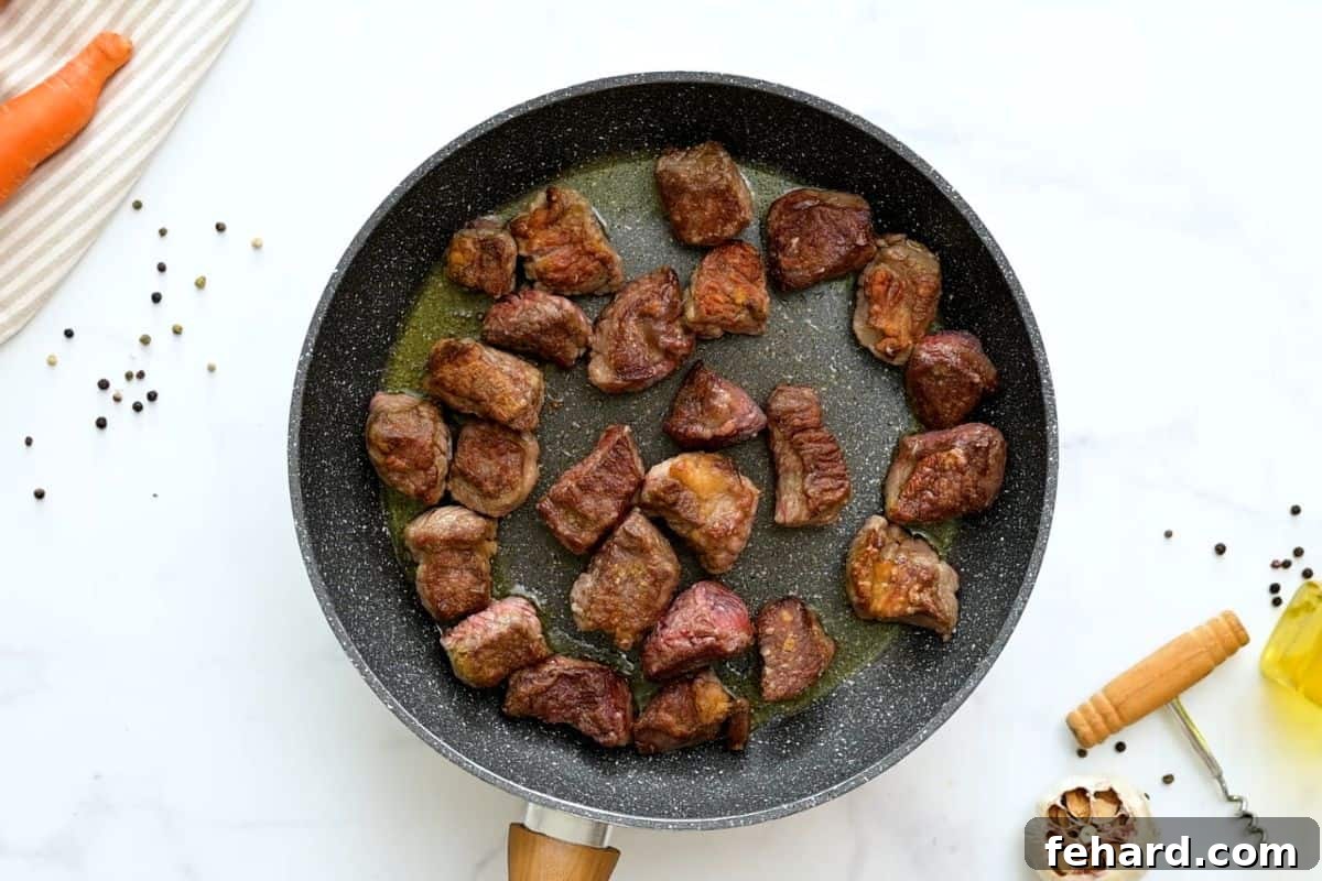 Close-up of perfectly browned chunks of floured chuck roast sizzling in a skillet, forming the flavor base for a hearty beef stew.