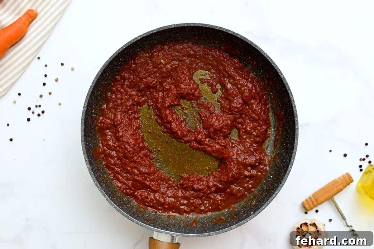 Red wine, sautéed onions, and rich tomato paste simmering together in a skillet, creating a deeply flavored base for beef stew.