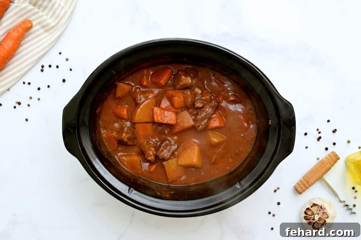 Slow-cooked Beef Stew bubbling gently in the crockpot, with tender potatoes and carrots visible, before the final thickening step.