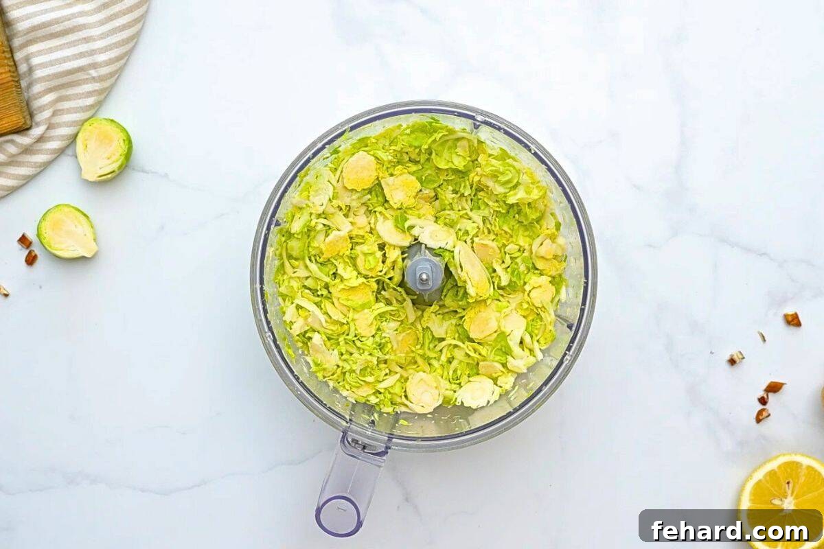 A food processor bowl filled with finely shaved Brussels sprouts, demonstrating the ease of preparation for this delicious salad.