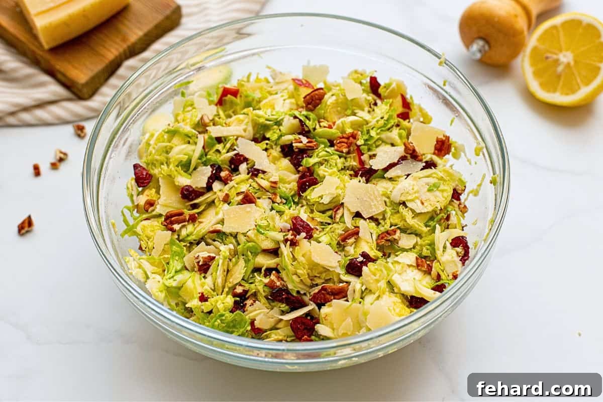 A large mixing bowl showcasing the fully assembled Shaved Brussels Sprouts Salad, beautifully tossed with honey lemon dressing, bright diced apples, vibrant dried cranberries, delicate shaved Parmesan, and crunchy chopped toasted pecans, presented elegantly and ready for serving.