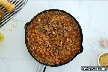 Fiesta Taco Rice Bake 5 Deep skillet with ground beef, pinto beans, uncooked rice, beef stock, and salsa before baking.
