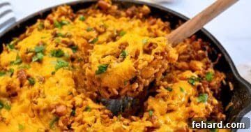 Fiesta Taco Rice Bake 8 Spoonful of taco rice casserole made with rice, beef, beans, and cheese coming out of deep skillet.