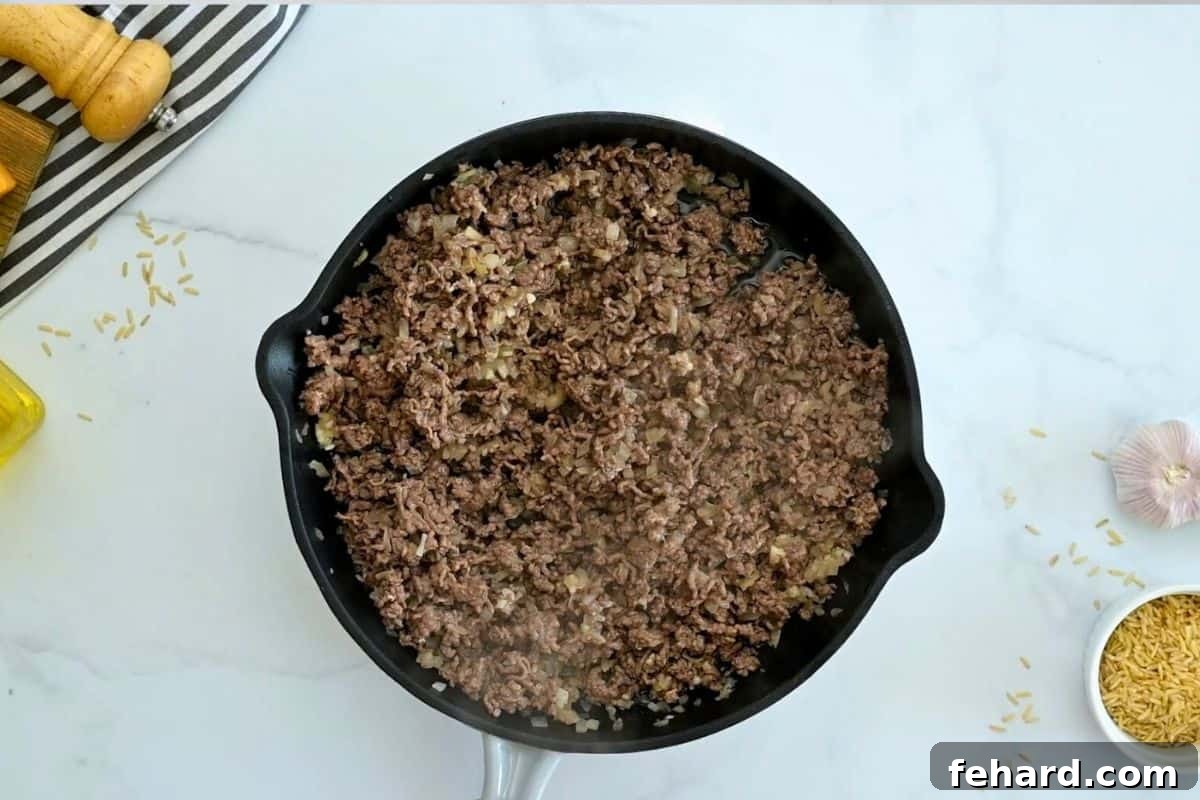 Taco Casserole with Rice Ground beef, minced onion, and garlic sautéing together in a large, deep oven-safe skillet.