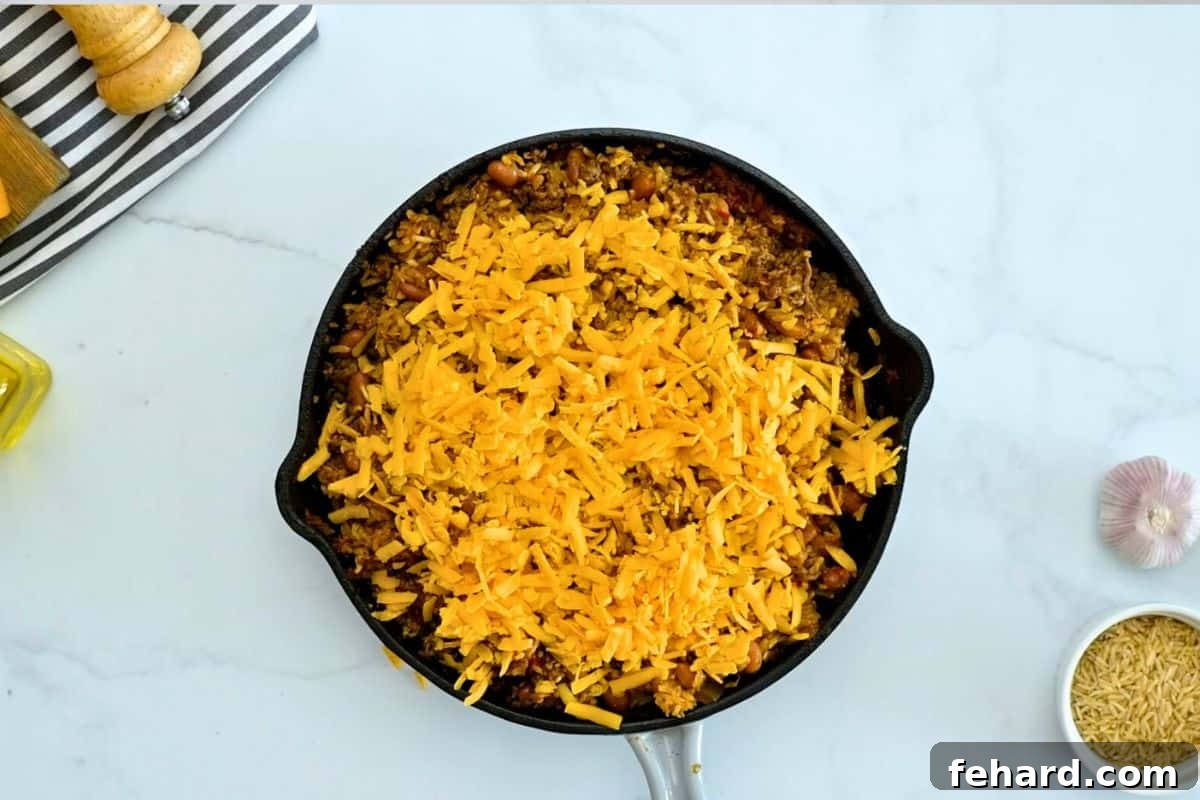 Taco Rice Baked Baked taco rice casserole in a deep skillet topped with a generous layer of shredded cheddar cheese, ready to be melted.