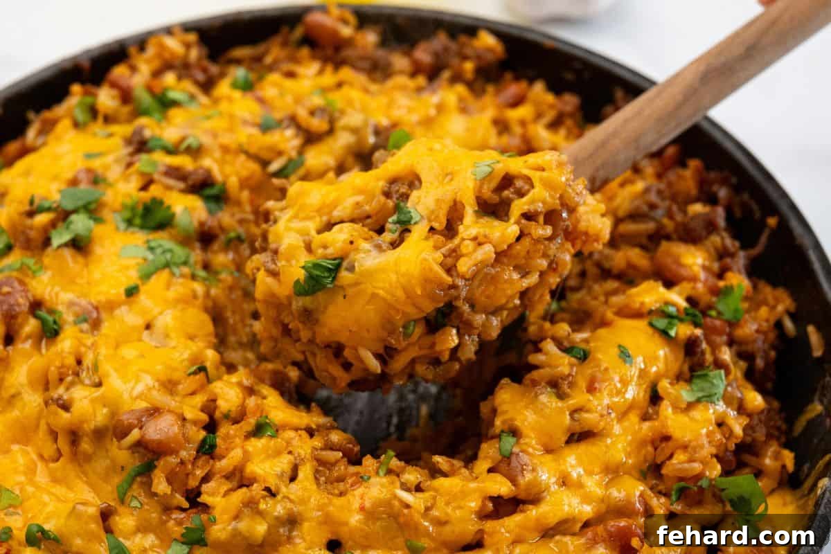 Easy Taco Rice Casserole A spoonful of warm, cheesy taco rice bake being scooped out of a deep skillet, ready to be served.