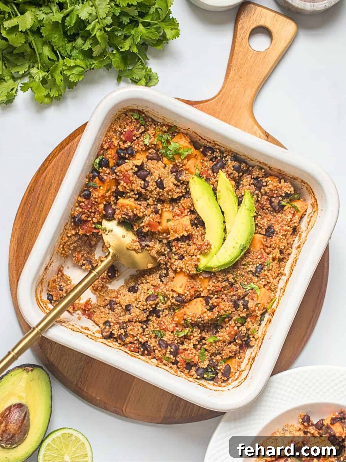 Vibrant Southwest Baked Quinoa with sweet potatoes, black beans, and diced tomatoes, garnished with fresh avocado and cilantro, alongside a wedge of lime in a white baking dish.