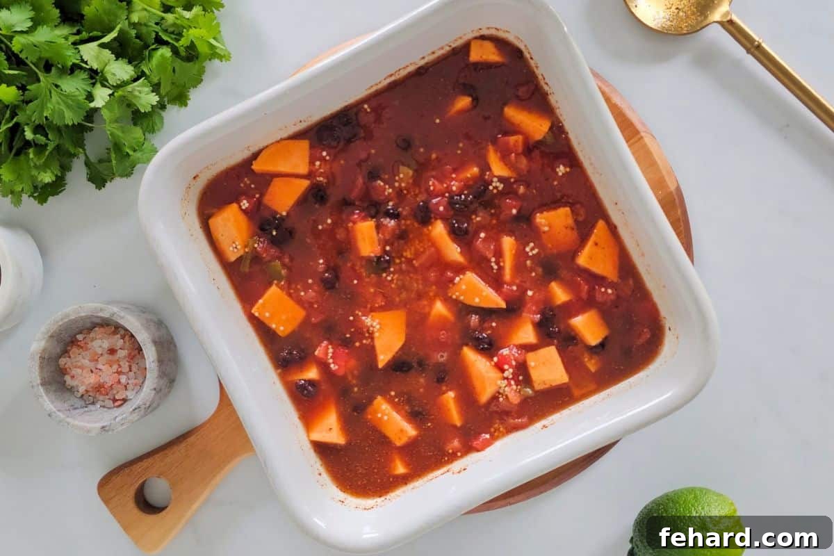 Unbaked Southwest Baked Quinoa ingredients including cubed sweet potatoes, canned black beans, diced tomatoes, vegetable broth, and taco seasoning, mixed in a white baking dish before baking.
