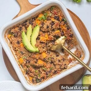 Baked quinoa with sweet potatoes, black beans, and diced tomatoes in white dish topped with avocado and cilantro with gold serving spoon taking out some.