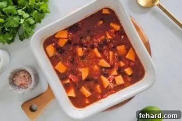 Quinoa with cubed sweet potatoes, canned black beans, diced tomatoes, vegetable broth, and taco seasoning in white dish before baking.