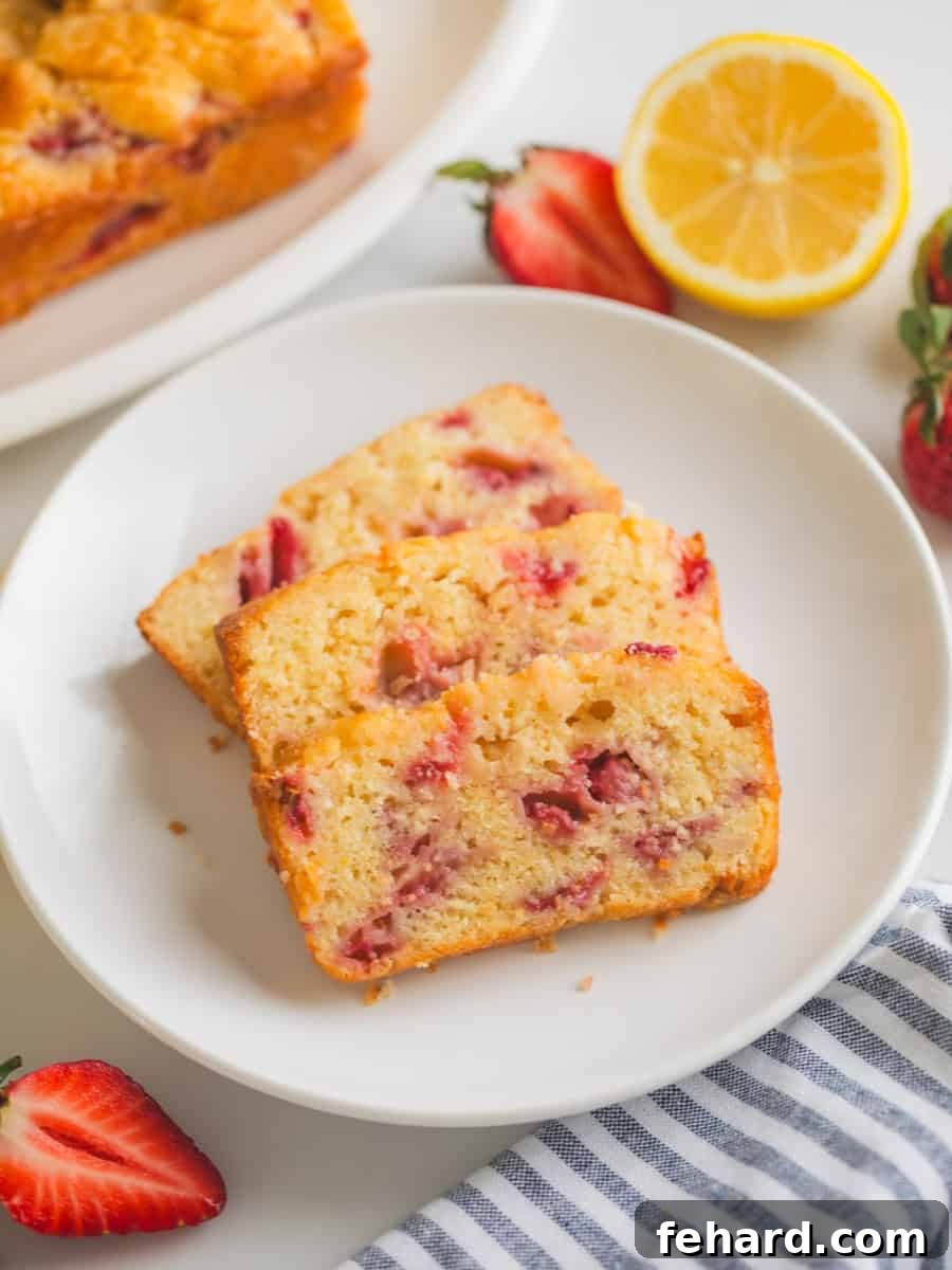 Slices of strawberry quick bread on white plate board next to fresh lemons and fresh strawberries.