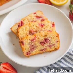 Slices of strawberry bread with lemon glaze on white plate board next to fresh lemons and fresh strawberries.