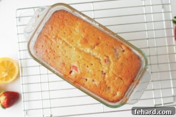 Baked strawberry loaf in pan on baking rack with holes poked in top for glaze to soak into bread.