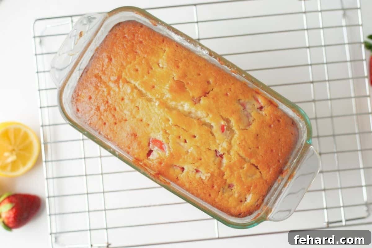 Baked strawberry loaf in pan on baking rack with holes poked in top for glaze to soak into bread.