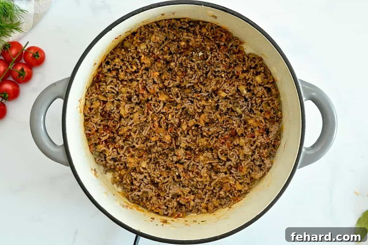 Richly browned ground beef infused with the aromatic flavors of paprika, onion powder, diced onion, and fresh garlic, all cooking together in a large Dutch oven, forming the foundational layer of our unstuffed cabbage rolls.