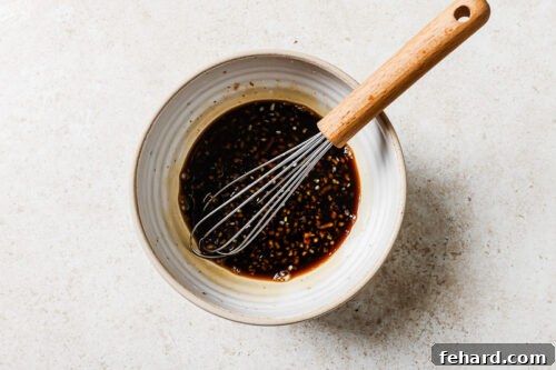 Homemade honey garlic sauce in a white bowl with a whisk, ready for glazing chicken.