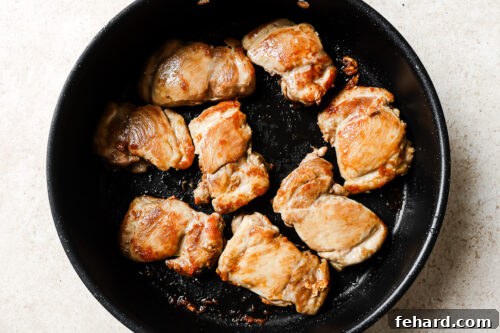 Raw chicken thighs searing in a cast iron skillet, developing a golden crust.