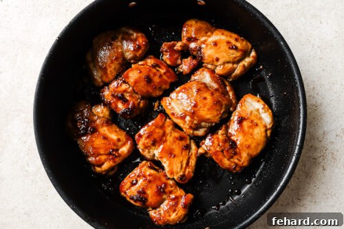Cooked honey garlic chicken thighs glistening in a skillet with the reduced sauce.