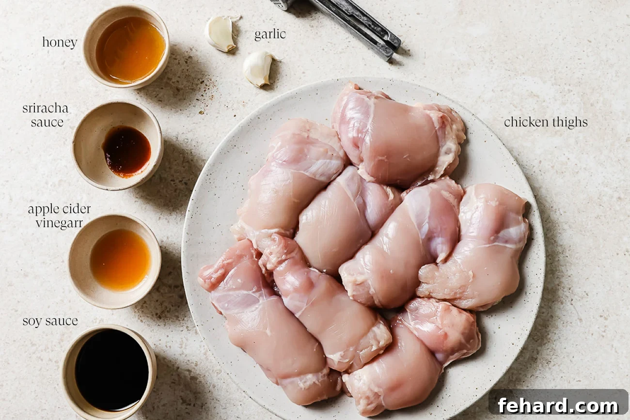 Raw boneless, skinless chicken thighs on a plate, surrounded by small bowls containing honey, sriracha, apple cider vinegar, soy sauce, and fresh minced garlic, all arranged on a light-colored kitchen counter.