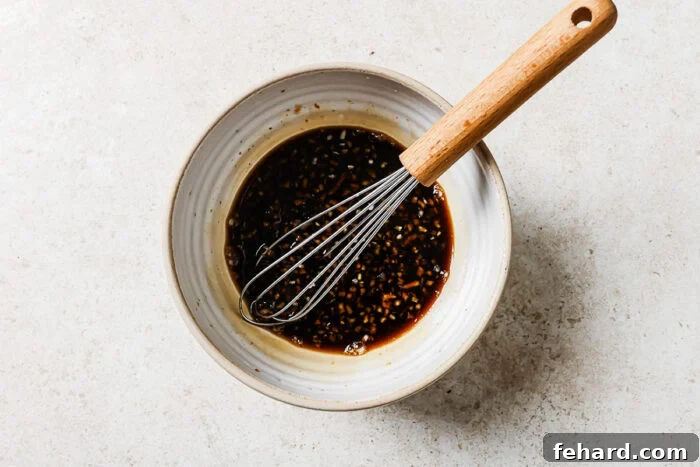 Homemade honey garlic sauce in a white bowl with a whisk, showing soy sauce, honey, garlic, apple cider vinegar, and sriracha blended smoothly.
