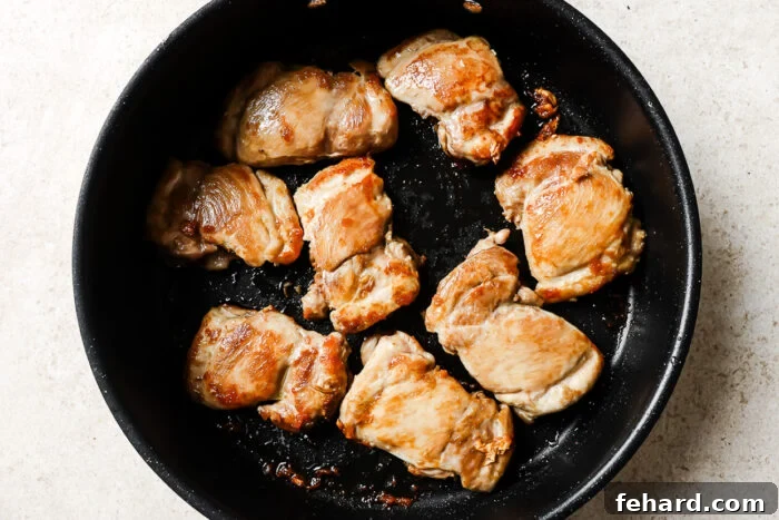 Raw boneless, skinless chicken thighs arranged in a single layer in a preheated cast iron skillet, ready to be seared to golden perfection.