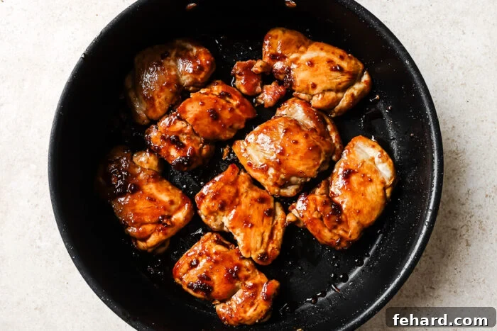 Honey garlic chicken thighs simmering in a cast iron skillet, enveloped in a rich, bubbling sweet and savory glaze.
