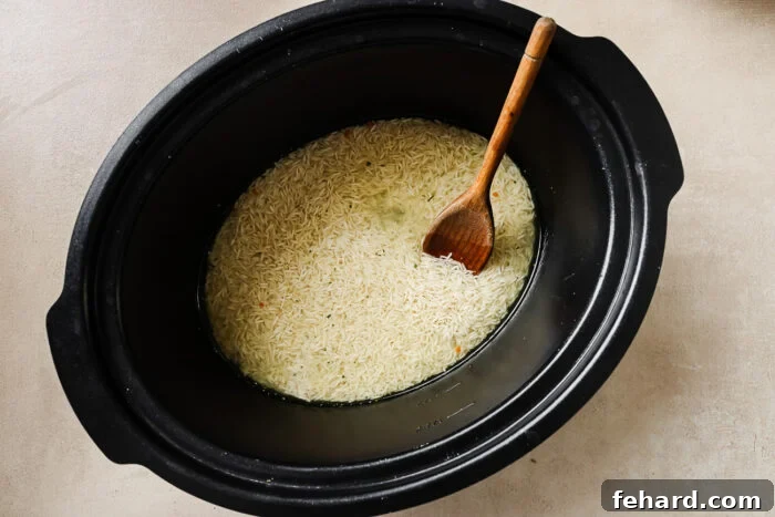 Easy Slow Cooker Chicken and Rice 4 Overhead view of uncooked long grain white rice at the bottom of a slow cooker pot, ready for broth.