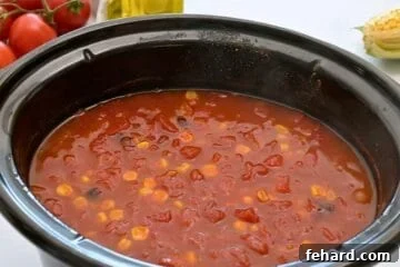 Slow cooker with cooked tortilla soup made with chicken breasts, beans, and corn, and a spiced tomato broth.