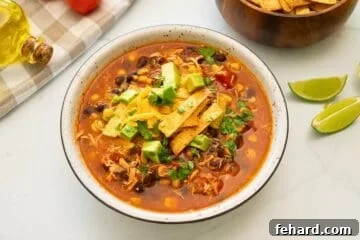 Bowl of Chicken Tortilla Soup topped with diced avocado, homemade tortilla strips, shredded cheese and minced cilantro.